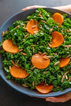 a person holding a bowl filled with kale and oranges