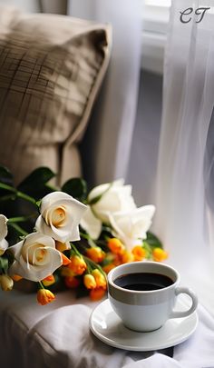 a cup of coffee next to some flowers on a bed with a pillow in the background