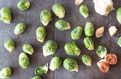 brussel sprouts, garlic and onions on a slate counter top with one peeled artichoke in the foreground