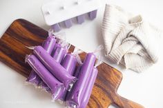 purple candles are on a wooden cutting board next to a white cloth and a pair of scissors