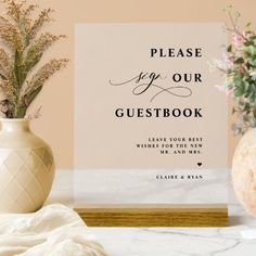 a white vase with flowers and a sign that says please keep our guestbook