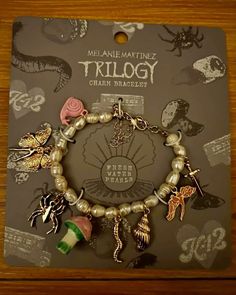 a bracelet with charms on it sitting in front of a card board that says trilogy