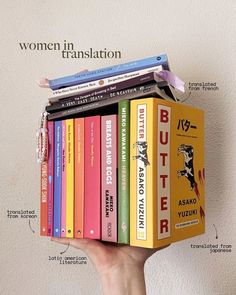 a person holding a stack of books in front of a wall with the words women in translation on it