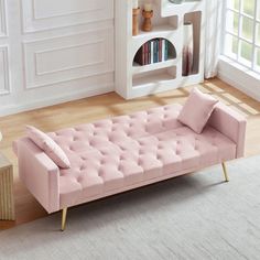 a pink couch sitting on top of a hard wood floor next to a book shelf