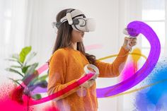 a woman in an orange sweater is using a virtual reality device to play with colorful streamers