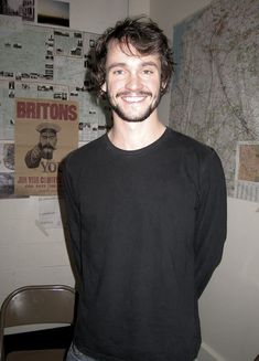 a man standing in front of a wall with posters on it and smiling at the camera