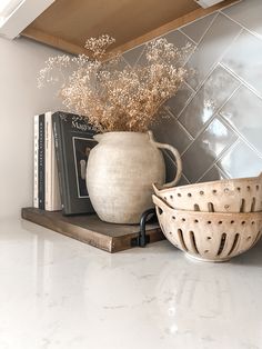 a white vase sitting on top of a counter next to a bowl and book shelf