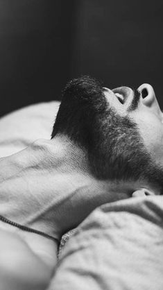 a black and white photo of a man laying in bed with his eyes closed looking up