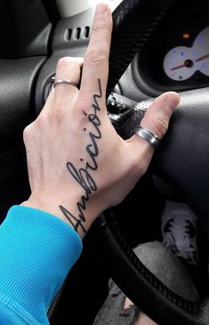 a person's hand on the steering wheel of a car that has writing on it