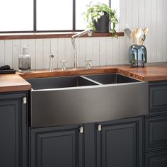 a large stainless steel kitchen sink with wooden counter tops and black cabinets in the background