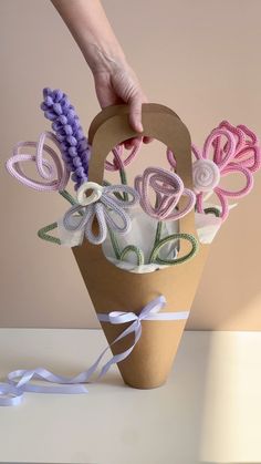 a hand holding a paper bag with flowers in it and ribbons on the bottom half