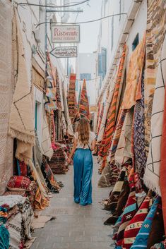 a woman is walking through an alley with lots of rugs on the floor and walls