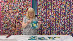 a woman holding up a cup in front of a wall with colorful squares on it