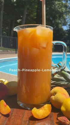 a pitcher filled with liquid sitting next to some fruit near a swimming pool and trees