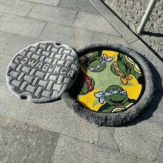 a manhole cover on the ground next to a sidewalk with an image of teenage mutants printed on it