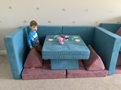 a young boy sitting on top of a blue couch next to a table with toys