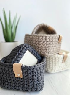 three crocheted baskets sitting on top of a white table next to a potted plant