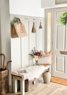 a white bench sitting in front of a door next to a basket filled with flowers