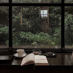 an open book sitting on top of a window sill next to a cup of coffee