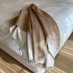 a blanket is folded on top of a bed with white sheets and wood flooring