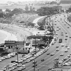 an old black and white photo of cars on the road in front of a beach