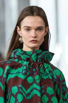 a woman with long brown hair wearing a green and black coat on the runway at london fashion week