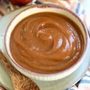 a bowl of peanut butter next to an apple and cinnamon on a plate with spoons