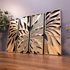 three wooden art pieces sitting on top of a table next to a potted plant