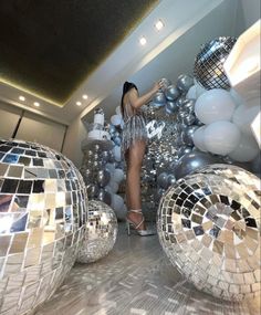 a woman standing next to disco balls in a room filled with silver and white balloons