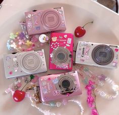 several cameras sitting on top of a white plate next to beads and cherries,