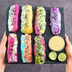 a person holding a tray with different types of sushi and dipping sauces on it