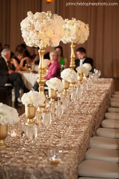 a long table topped with gold vases filled with white flowers