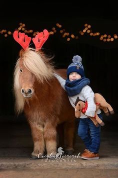 a small child is standing next to a miniature horse with antlers on its head