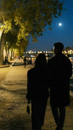 two people walking down the sidewalk at night