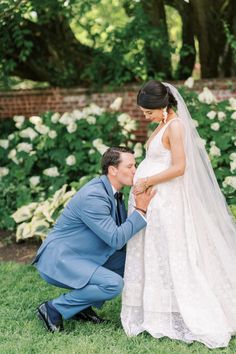 a man kneeling down next to a woman in a wedding dress and holding her hand