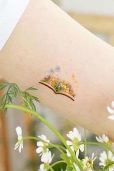 a woman's arm with flowers on it and a small book in the middle