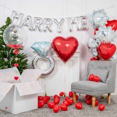 a chair and balloons in front of a christmas tree with the words marry me on it