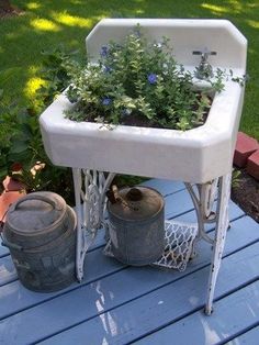 a white sink sitting on top of a wooden table next to two buckets filled with flowers