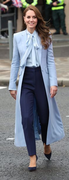 a woman in blue coat and pants walking down the street with other people behind her