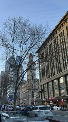 cars are parked on the street in front of tall buildings and trees with no leaves