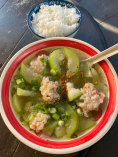 a bowl filled with meat and vegetables next to rice on top of a wooden table