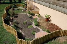 a garden area with plants and rocks in the ground next to a fenced off building