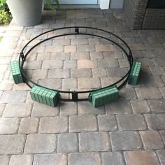 four green benches sitting in the middle of a circle on a brick patio next to a potted plant