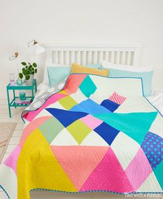 a bed with a colorful quilt on top of it next to a small table and potted plant