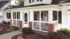 a white house with red brick and green shutters on the front porch, along with two large windows