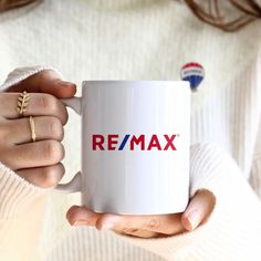 a woman holding a white coffee mug with the word re / max on it's side