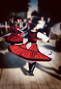 two women in red and white dresses are dancing on the street with people walking by