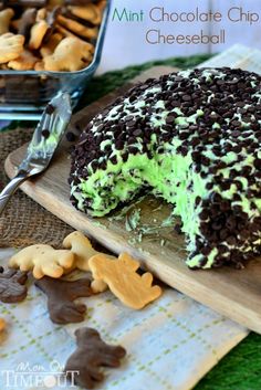 a chocolate chip cheesecake with green frosting on a cutting board next to cookies