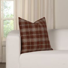 a brown and white plaid pillow sitting on top of a couch next to a window