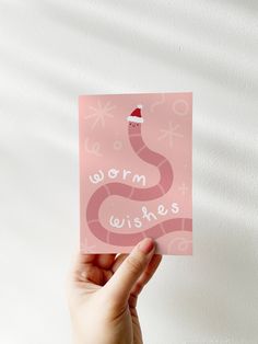 a hand holding up a pink card with the words worm wishes on it and a santa hat